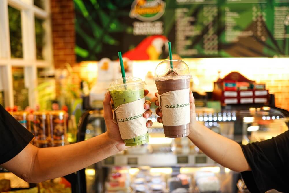 Two people share iced coffee and tea drinks at a Café Amazon.